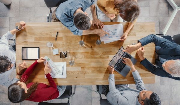 Startup Meeting Room: Team of Entrepreneurs sitting at the Conference Table Have Discussions, Solve Problems, Use Digital Tablet, Laptop, Share Documents with Statistics, Charts. Top View Shot